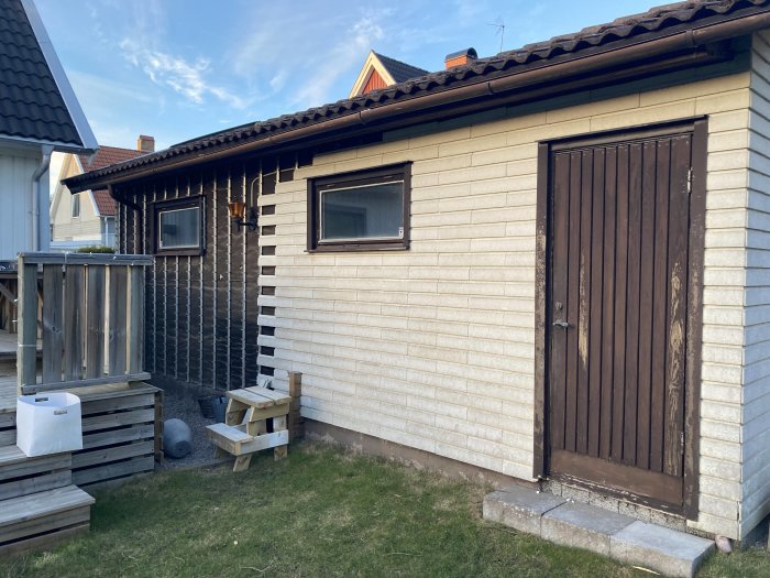 Garage med vit fasad och brunt hängtegel före renovering med stående z-panel.