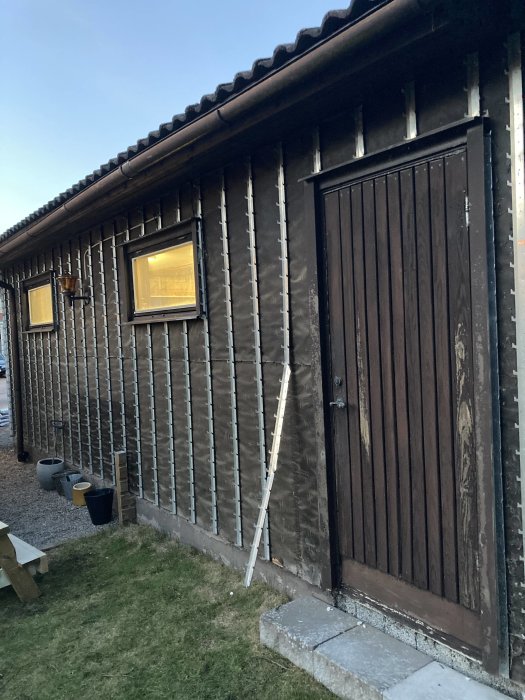 Garage med mörkbrunt hängtegel och en stängd dubbelport. En stege lutar mot väggen inför renovering.