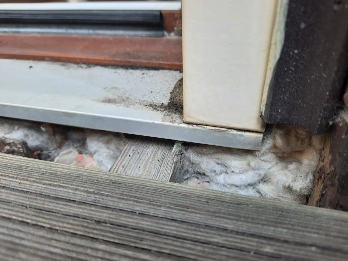 Närbild på en balkongdörrs tröskel med isolering synlig och en kil som ska justeras.
