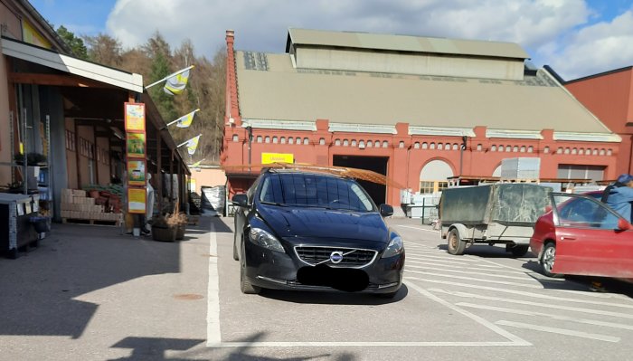 Bil på parkering med armeringsnät på taket framför byggnadsmaterialhandel.