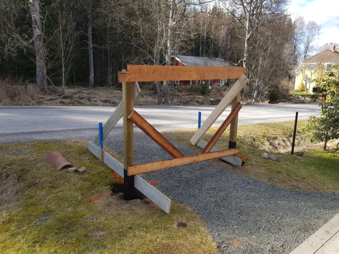 Nybyggda trägrindstolpar i en trädgård, nära en grusgång och väg, med tillfälliga stöd.