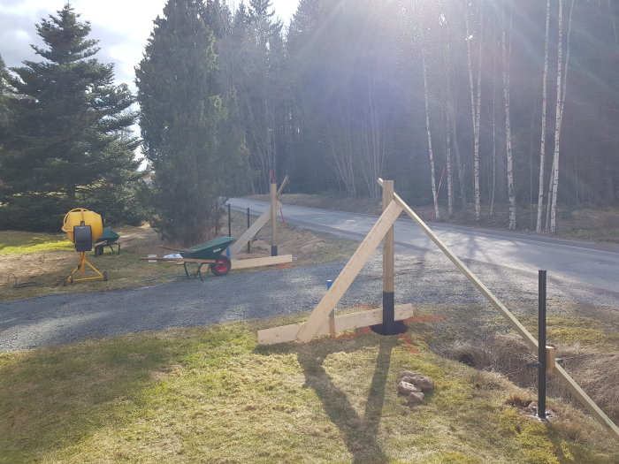 Nyligen uppsatta trägrindstolpar vid en väg med byggmaterial och verktyg i bakgrunden.