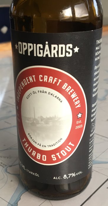 Flaska med Oppigårds Thurbo Stout öl, 8,7% alkoholvolym, stående på ett bord.