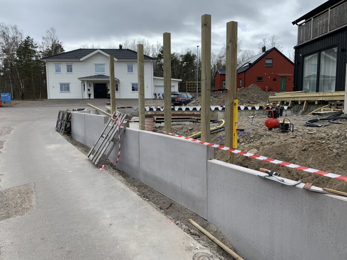 Installation av staketstolpar på L-stöd vid ett byggprojekt, med verktyg och hus i bakgrunden.