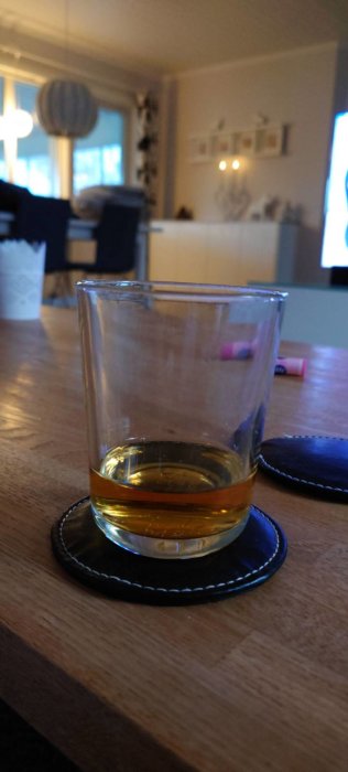 Ett whiskyglass med lite dryck på ett bord i ett suddigt vardagsrum.