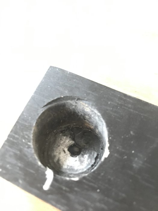 Närbild på en metallplatta med ett borrat hål där borrhuvudet verkar ha fastnat eller brunnit fast.