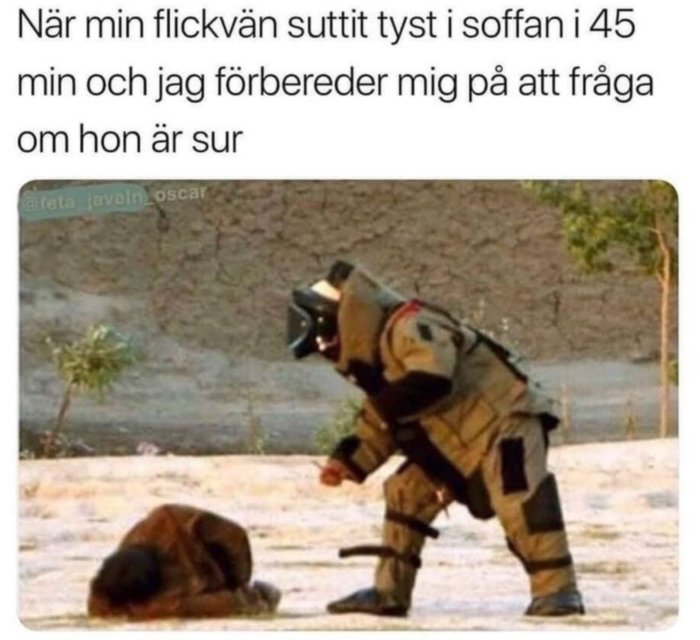 Person i bombdräkt närmar sig försiktigt en sittande apa på marken.