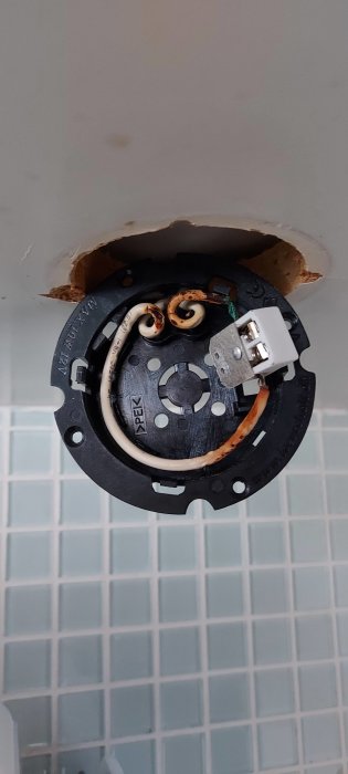 Äldre halogen downlight under köksskåp med synliga, skadade kablar och öppen armatur.