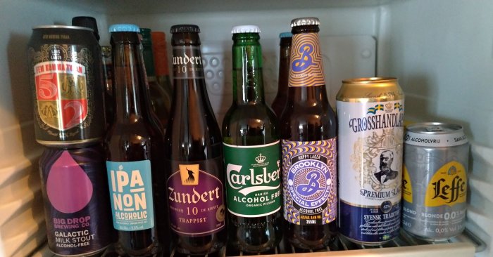 Olika sorters ölflaskor och ölburkar, vissa alkoholfria, i ett kylskåp.
