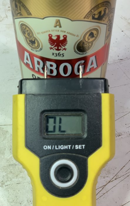 Fuktmätare visar "OL" framför en Arboga ölburk på en arbetsyta.