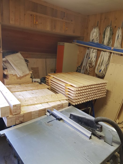 Verkstad med kapsåg och staplar av träspjälor kapade i 52,5 grader för staketprojekt.