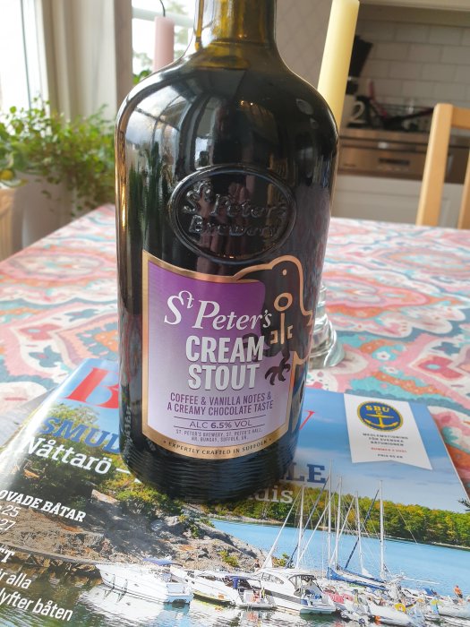 Flaska av St. Peter's Cream Stout på en tidning med båtar, på ett köksbord.