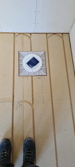 Installation av ett golvbrunnsgaller på ett kaklat badrumsgolv med synliga fötter.