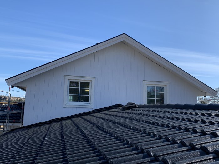 Gavel på hus med ny panel och fönster, sedd ovanifrån takpannor mot klarblå himmel.