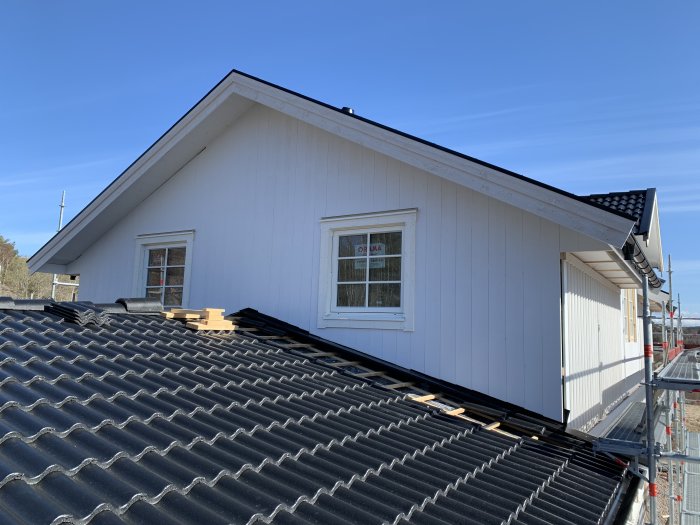 Nymålad gavel med vit panel på hus under byggnation, synlig takstol och byggmaterial på tak.