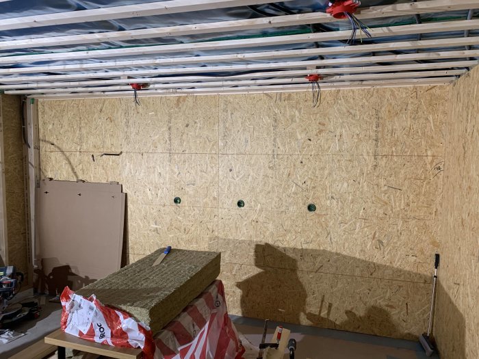 OSB-panel installerad på köksvägg med synliga isoleringsmattor och elinstallationer under arbete.