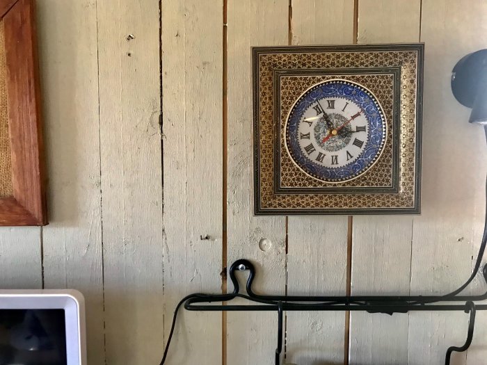 Kello koristeellisessa kehyksessä roikkuu seinällä, joka on peitetty raakalaudalla.