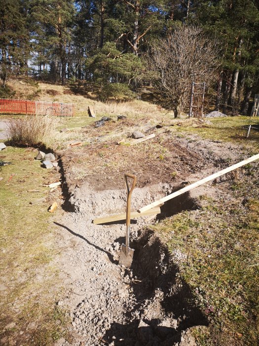 Trädgårdshörn med röjda rester av täckplast och spade i uppgrävd jord framför en slänt.