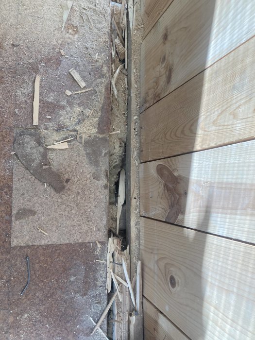 Beskrivning av pågående renoveringsarbete där ny träpanel möter ett gammalt golv nära en väggkant.