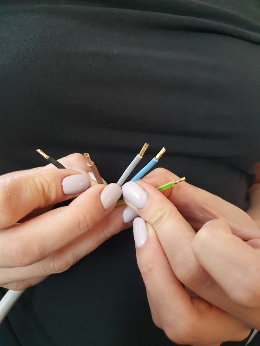 En person håller en perilexkabel med fem avskalade ändar för installation av induktionshäll.