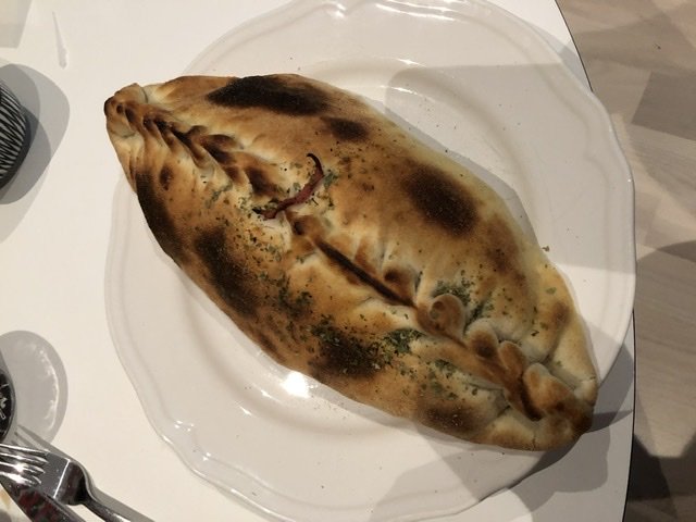 Nylagad calzone-pizza med gyllenbrun yta på en vit tallrik.
