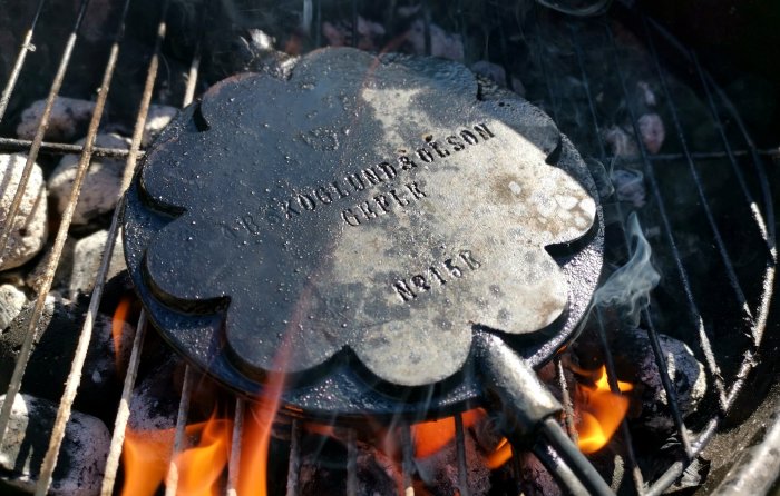 Rökutvecklare i form av ett blomliknande metallföremål på en glödande kolbädd i en grill.