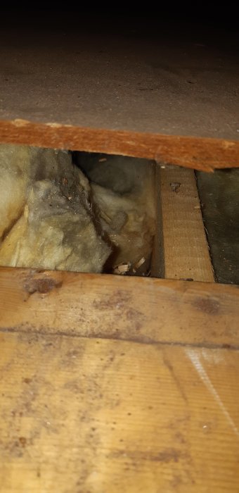 Utsikt genom en upplyft golvplatta som visar en bjälkstruktur och isolering, vilket ifrågasätter väggens bärighet.