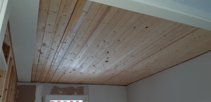 Trätak med synliga bjälkar längs med rummet och spår efter borttagen vägg.