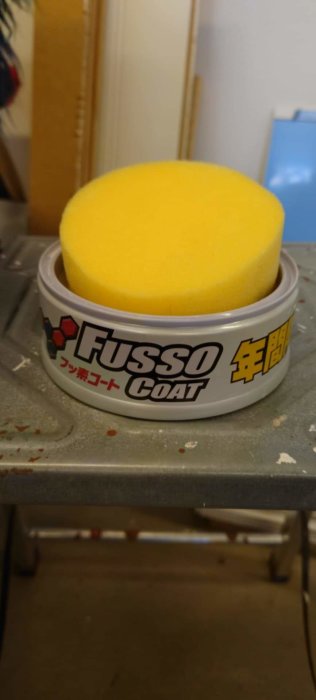 Soft99 Fusso Coat bilvaxburk med skumtvättsvamp på ett dammigt arbetsbord.