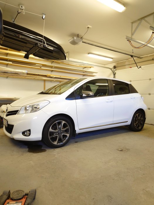 Ren och vaxad vit bil med sommardäck i ett garage, verktyg synliga på golvet.