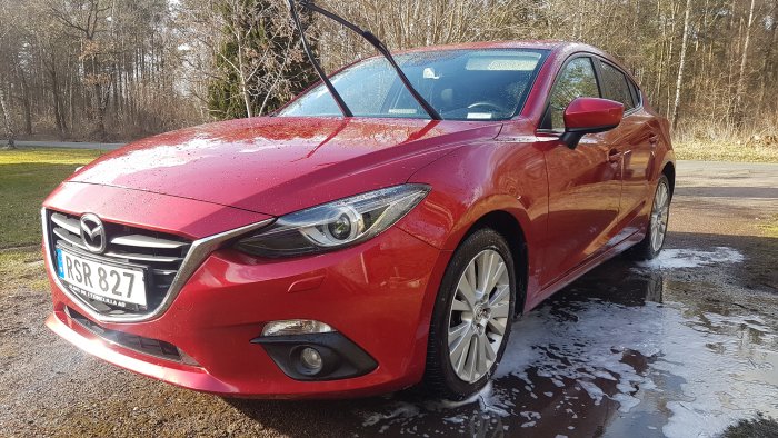 Röd glänsande Mazda tvättas med vatten, dörren öppen, skum på marken.