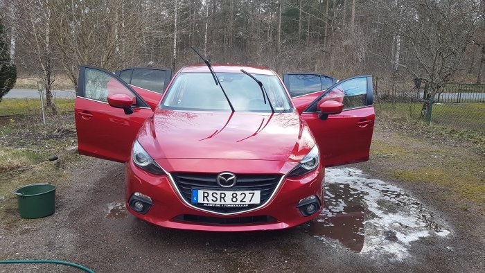 Röd Mazda med alla dörrar öppna under tvätt med vatten och hink synlig.