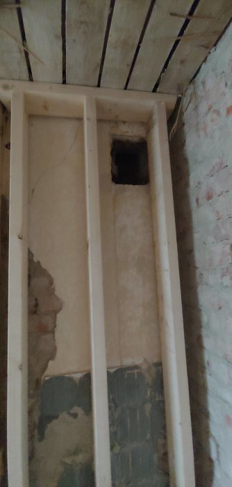 Ventilationshål i skorsten med träreglar och isolering runt, i en halvfärdig väggkonstruktion.