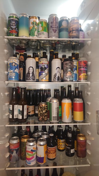 Kylskåp fullt av olika sorters ölburkar och flaskor på hyllor.