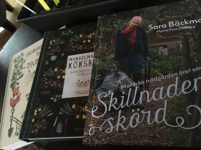 Trädgårdsböcker och kokbok för självhushållning är utspridda framför krukor med plantor.