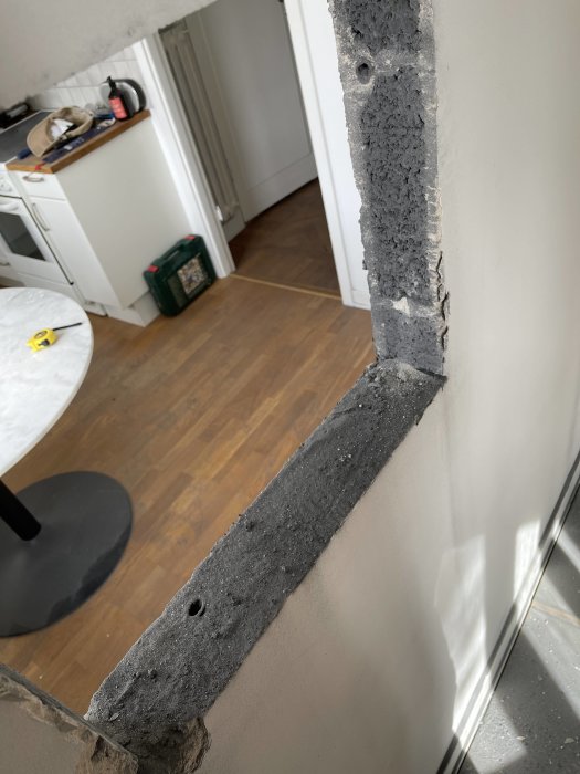 Delvis nedbruten vägg mellan kök och vardagsrum i lägenhet, stenblock och puts synligt med kapad elsladd.