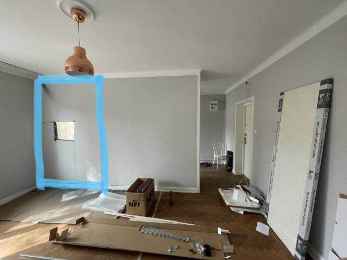 En oinredd lägenhet där en stenblocksvägg markerad med blå tejp för planerad öppning mellan kök och vardagsrum.