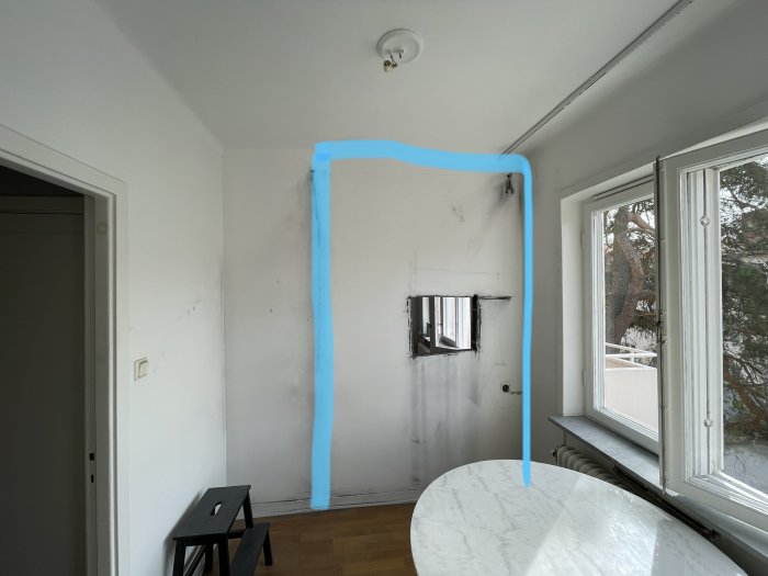 Inomhusvy av en vägg i en lägenhet med blå tejp som markerar planerad öppning, och en kapad elsladd synlig.
