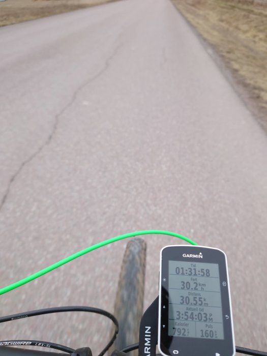 Cyklistens perspektiv med cykeldator visande tid och statistik på styret, asfalterad väg i bakgrunden.