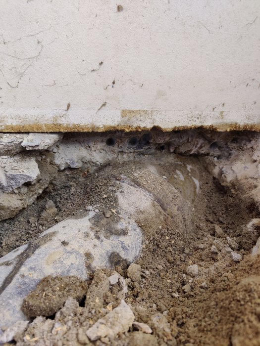 Avloppsrör som sticker ut från källarvägg med uppbrutet betonggolv och grus runtomkring.