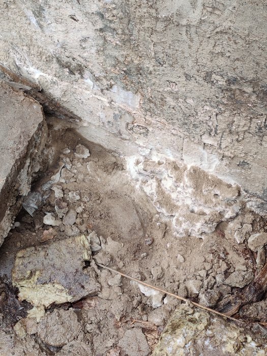 Avbilat källargolv och stenmaterial vid yttervägg under dräneringsarbete.