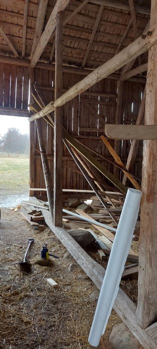 Inredning av lada med träbjälkar, stödsträvor och verktyg, inför renovering till verkstad.