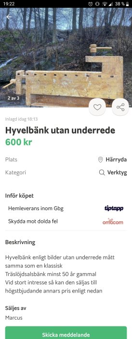 Begagnad trähyvelbänk utan underrede placerad framför lövträd och buskage.