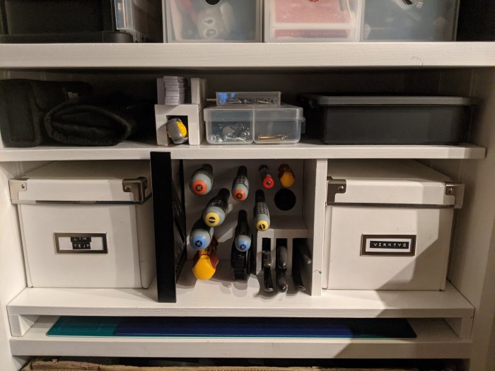 Organiserad hylla med verktygslådor och hängande skruvmejslar och tänger.