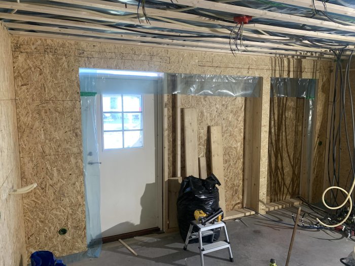 Garage under renovering med osb-skivor på väggar, reglar runt dörr och port samt ogjort tak.