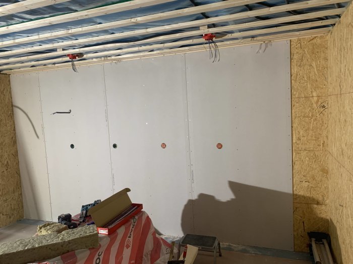 Inre hörn av ett garage under renovering med nya gipsväggar, osb-skivor och takbjälkar synliga.