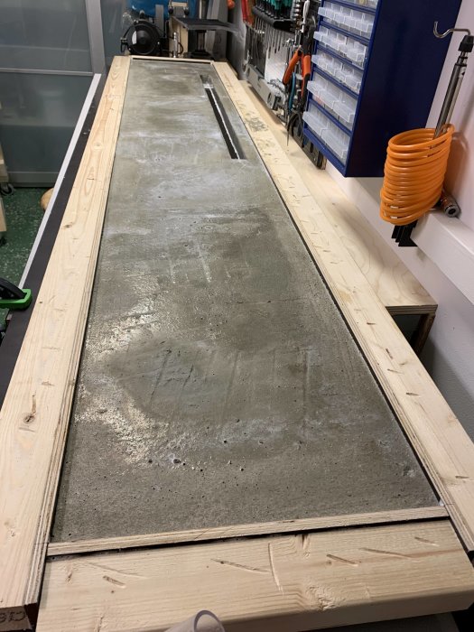 Nyformad betongplatta omgiven av träformar på verkstadsbänk, redo för avformning och slipning.