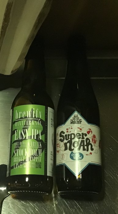 Två ölflaskor, Brewfys Easy IPA och Cool Brews Super Ale, på en mörk yta.