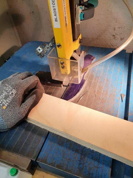 Bandsåg i arbete som skär ut en knivprofil från en metallplåt med träbräda som stöd.