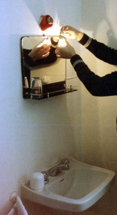 Två händer håller en lös elsladd mot en glödlampa ovanför en handfatsspegel.